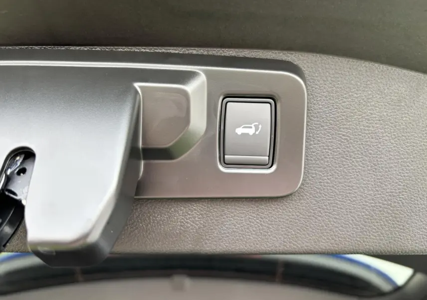 Gros plan sur le bouton d'ouverture mains-libres du hayon du Renault Austral bleu Iron Metal, intérieur du coffre visible.