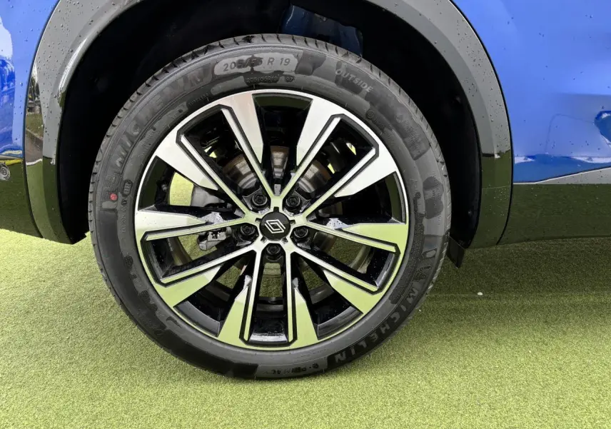 Gros plan sur la jante alliage 19 pouces Komah diamantée noire du côté gauche du Renault Austral bleu Iron Metal.