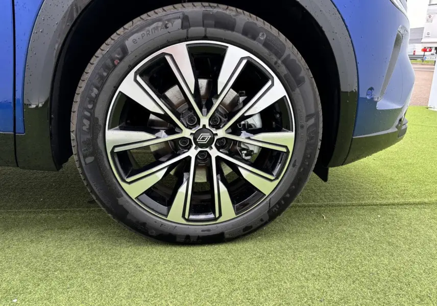 Gros plan sur la jante alliage 19 pouces Komah diamantée noire du côté avant droit du Renault Austral bleu Iron Metal.