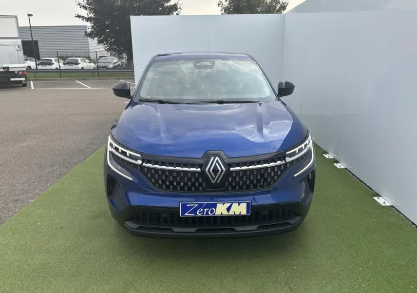 Vue frontale d'un Renault Austral bleu Iron Metal avec calandre à damier et feux LED distinctifs allumés.