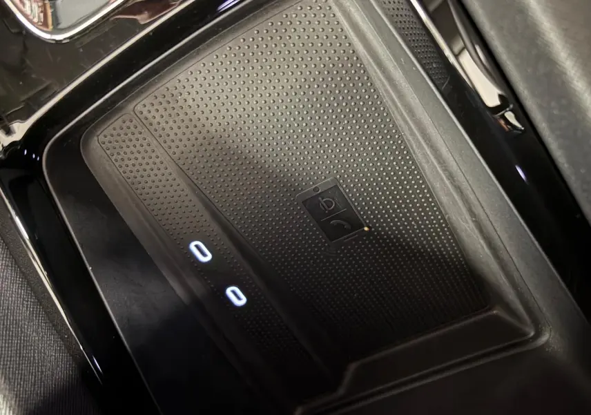 Gros plan sur le chargeur sans fil noir avec indicateurs lumineux dans le compartiment central d'une Skoda Octavia Combi gris argent 2023.