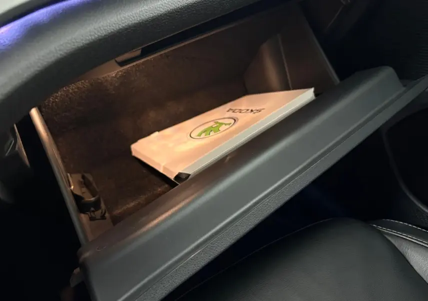 Boîte à gants ouverte côté passager d'une Skoda Octavia Combi gris argent 2023 avec manuel visible à l'intérieur.