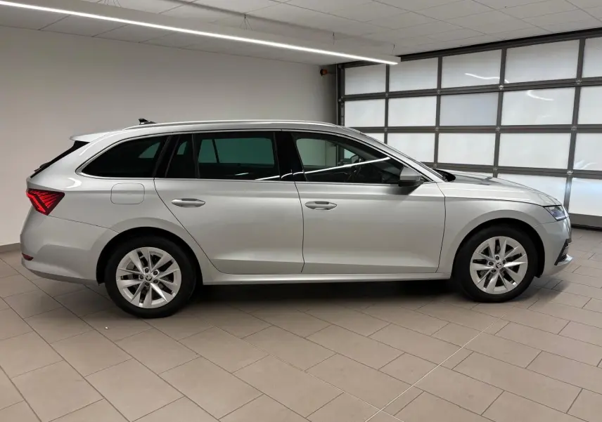 Skoda Octavia Combi 2023 gris argent vue de profil côté gauche dans un garage lumineux avec jantes alliage.