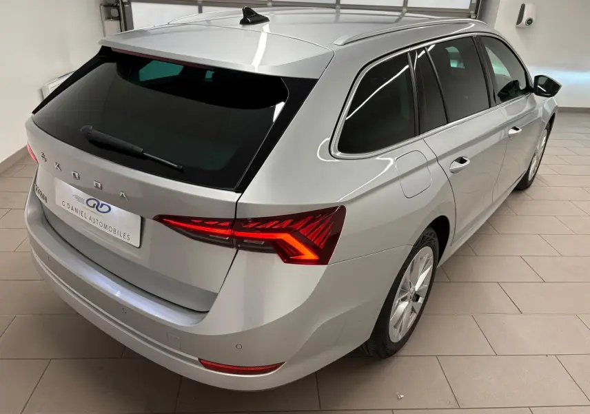 Vue 3/4 arrière droite d'une Skoda Octavia Combi gris argent 2023 avec feux arrière LED allumés dans un garage.