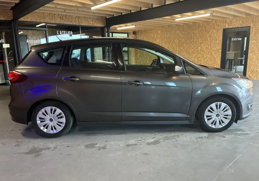 Profil côté gauche d'un Ford C-MAX gris 2015 garé en intérieur, avec jantes argentées et cinq portes visibles.