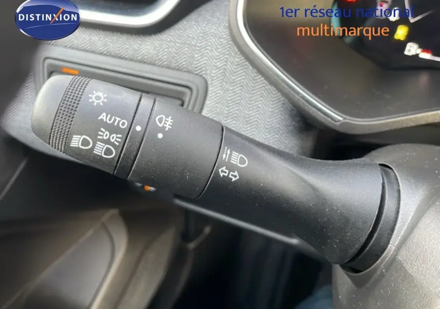 Gros plan sur la commande des feux et clignotants noire dans l’habitacle d’une Renault Clio rouge Désir Métal.