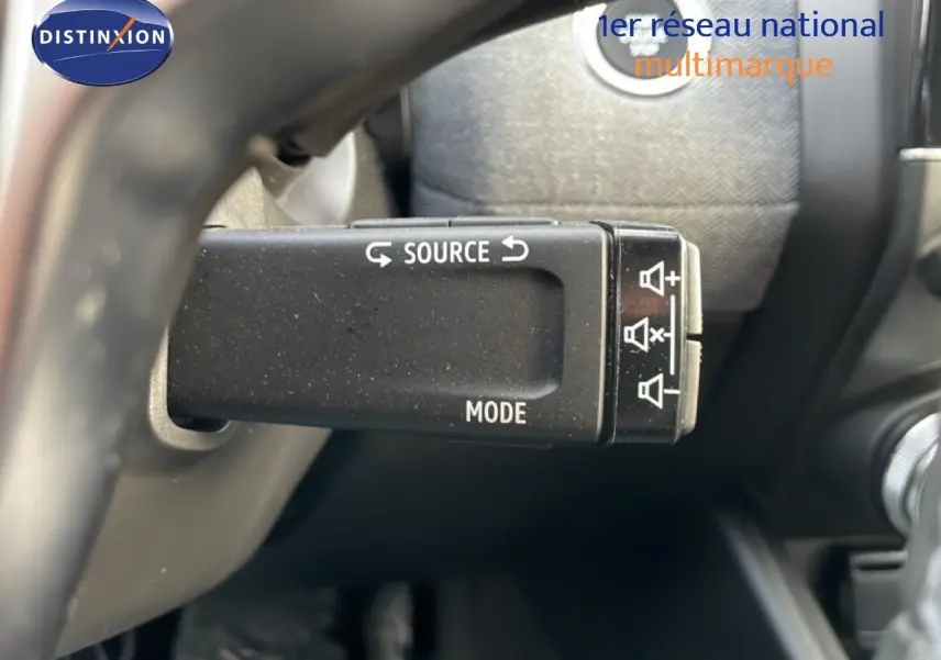 Gros plan sur la commande au volant de la Renault Clio rouge Désir Métal, mettant en valeur les boutons source et mode.