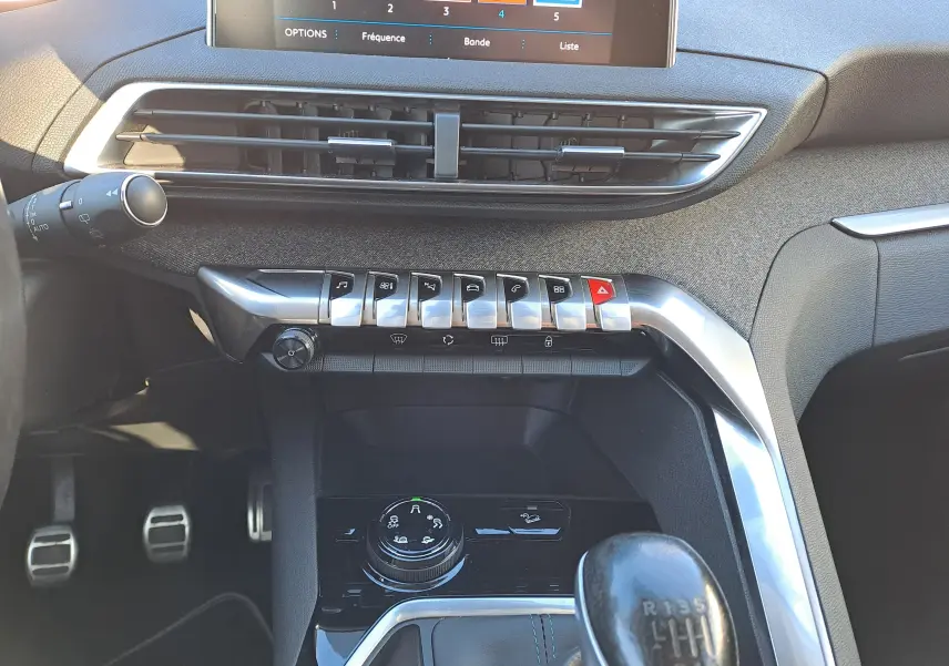 Vue intérieure centrée sur la console centrale et levier de vitesse manuelle d’un Peugeot 5008 gris, avec commandes et écran tactile visibles.