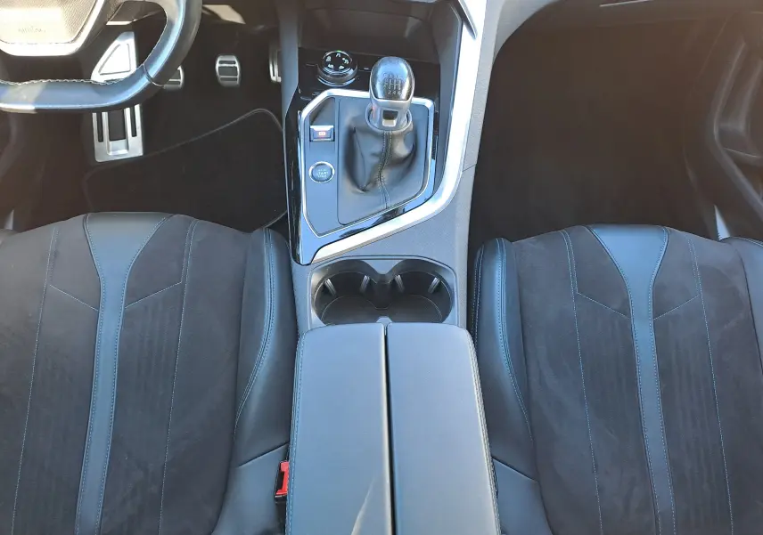 Vue intérieure centrée sur la console centrale et les sièges avant en cuir noir du Peugeot 5008 gris, boîte manuelle.