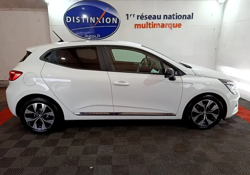 Profil droit d'une Renault Clio Business TCe 100 GPL blanche, avec jantes alliage et rétroviseurs noirs dans un showroom.