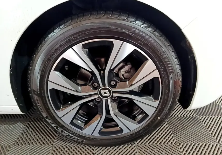 Gros plan sur la roue avant gauche d'une Renault Clio blanche avec jante alliage bicolore au design moderne.