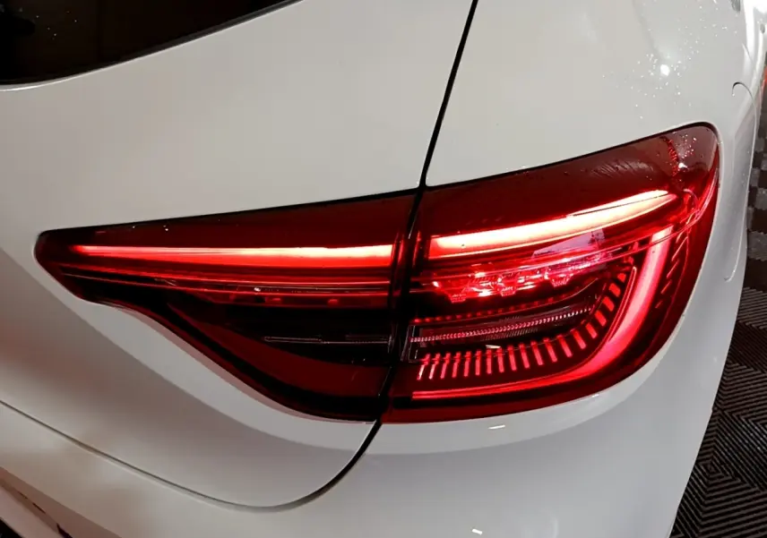Feu arrière droit allumé sur Renault Clio Business blanc, vue rapprochée du coffre et de la carrosserie.