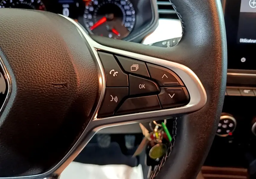 Gros plan sur les commandes multifonctions à droite du volant cuir noir de la Renault Clio Business TCe 100 GPL blanche, tableau de bord en arrière-plan.