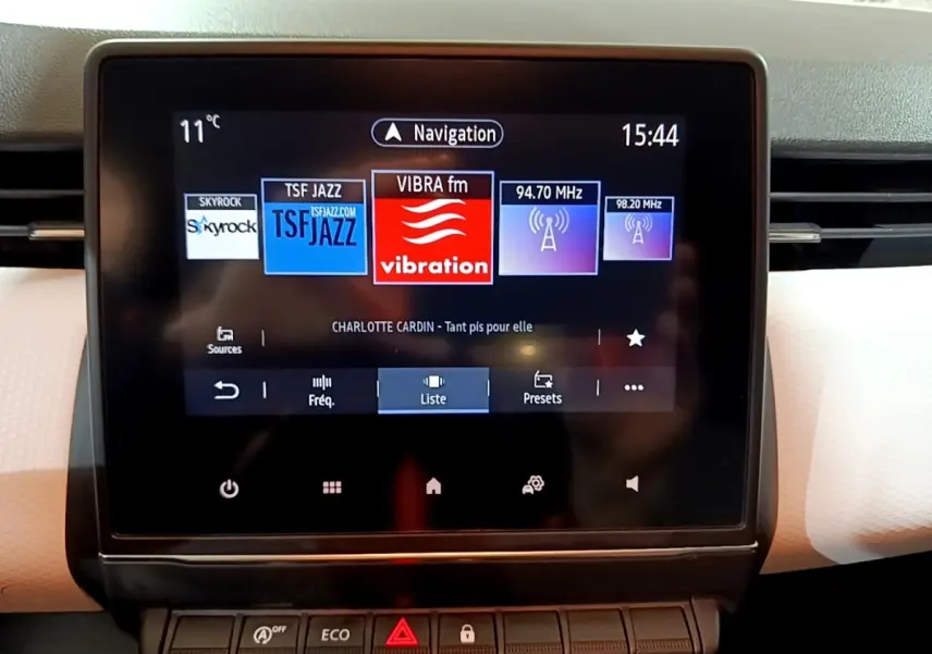 Écran tactile central affichant la radio et la navigation dans l'habitacle clair d'une Renault Clio blanche 2023.