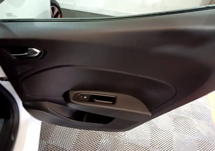 Vue rapprochée de la porte intérieure côté gauche d’une Renault Clio blanche, avec poignée et commande de fenêtre noire.