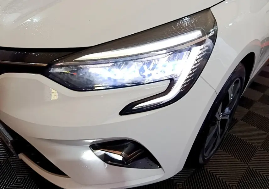 Gros plan sur l'avant droit blanc d'une Renault Clio 2023 avec phares LED allumés et jante noire visible.