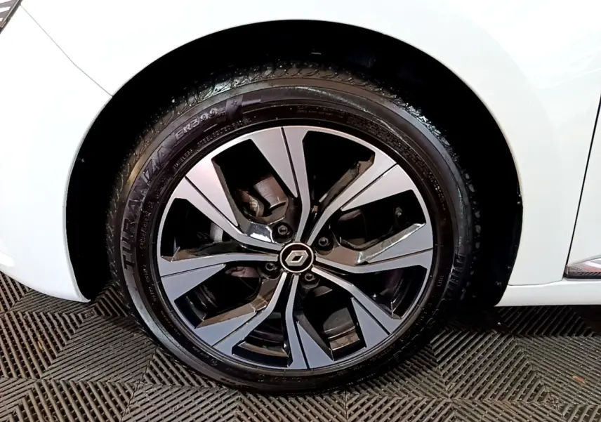 Gros plan sur la roue avant gauche d’une Renault Clio blanche avec jante alliage au design moderne bicolore.