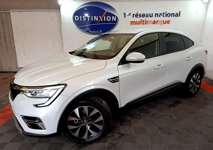 Renault Arkana blanc en 3/4 avant droit, SUV hybride avec jantes noires et phares LED allumés.