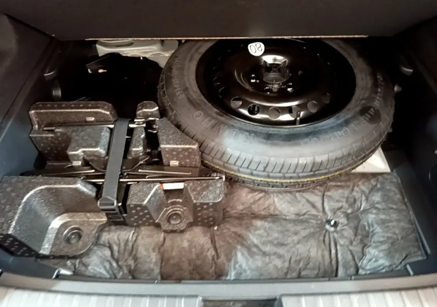 Vue du coffre ouvert du Renault Arkana blanc 2023, montrant la roue de secours et les outils de bord rangés.