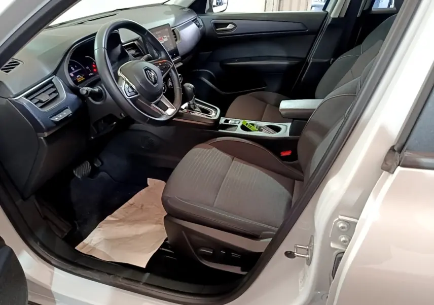 Vue intérieure côté conducteur d'une Renault Arkana blanc, montrant le volant cuir, tableau de bord et sièges tissu gris.