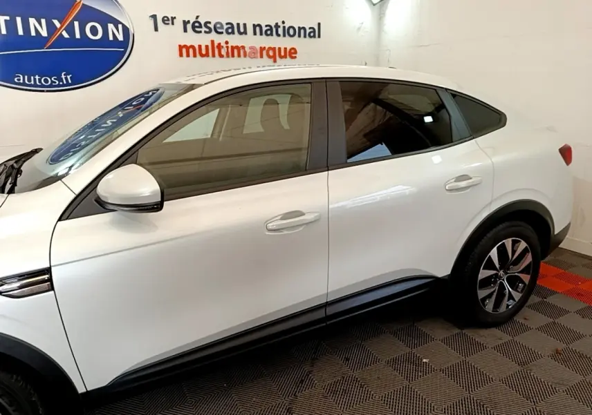 Profil côté gauche du Renault Arkana blanc 2023 avec jantes bicolores et lignes de caisse marquées.