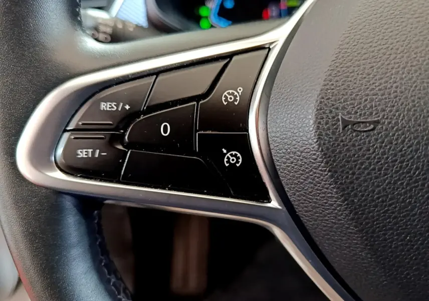 Gros plan sur les commandes de régulateur de vitesse au volant cuir du Renault Arkana blanc, version Evolution E-Tech.