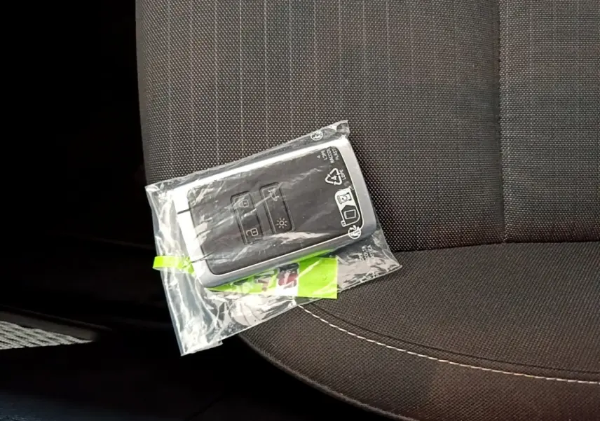 Gros plan sur la clé Renault Arkana Evolution E-Tech blanche posée sur un siège tissu gris foncé.