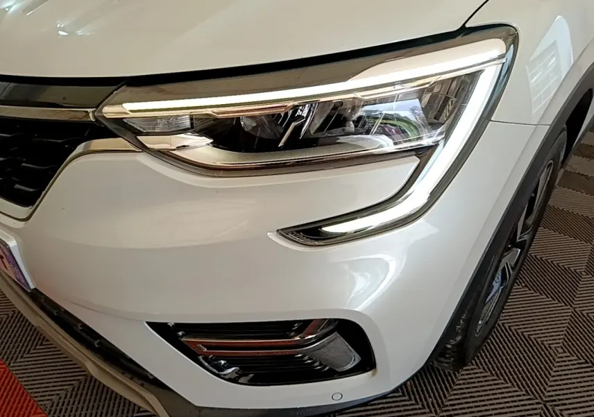 Gros plan sur l'avant droit blanc du Renault Arkana 2023, mettant en valeur le phare LED et la calandre noire.