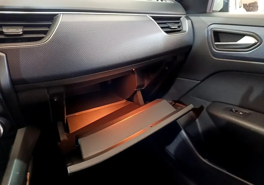 Vue intérieure côté passager du tableau de bord noir du Renault Arkana avec boîte à gants ouverte et éclairage intérieur.