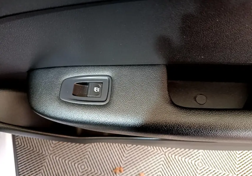 Détail de la commande de lève-vitre électrique sur la porte intérieure noire d’un Renault Arkana blanc 2023.