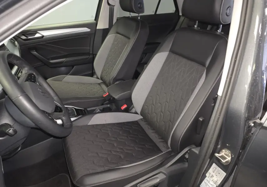 Vue intérieure côté conducteur du Volkswagen T-Roc 2025 avec sièges tissu noir et gris et accoudoir central.