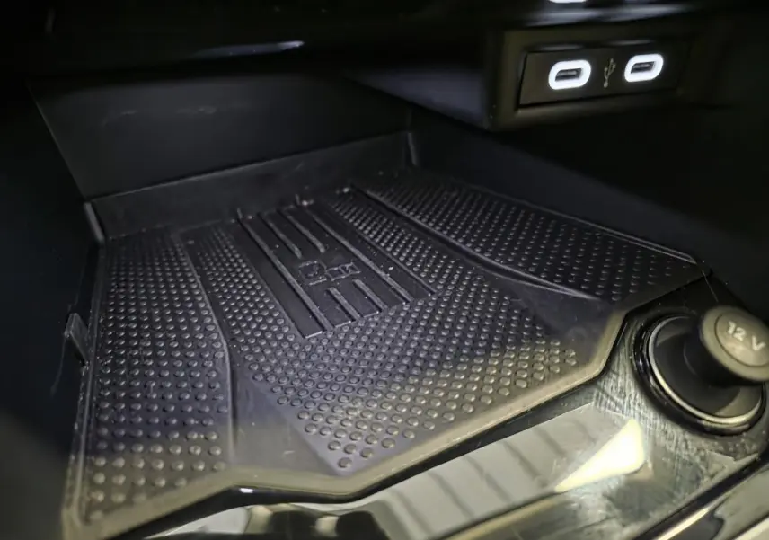 Gros plan sur le compartiment de rangement avant du Volkswagen T-Roc gris, avec ports USB-C et prise 12V visibles.