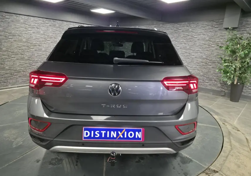 Vue arrière d'un Volkswagen T-Roc gris métallisé 2025 avec feux LED allumés et attelage démontable.