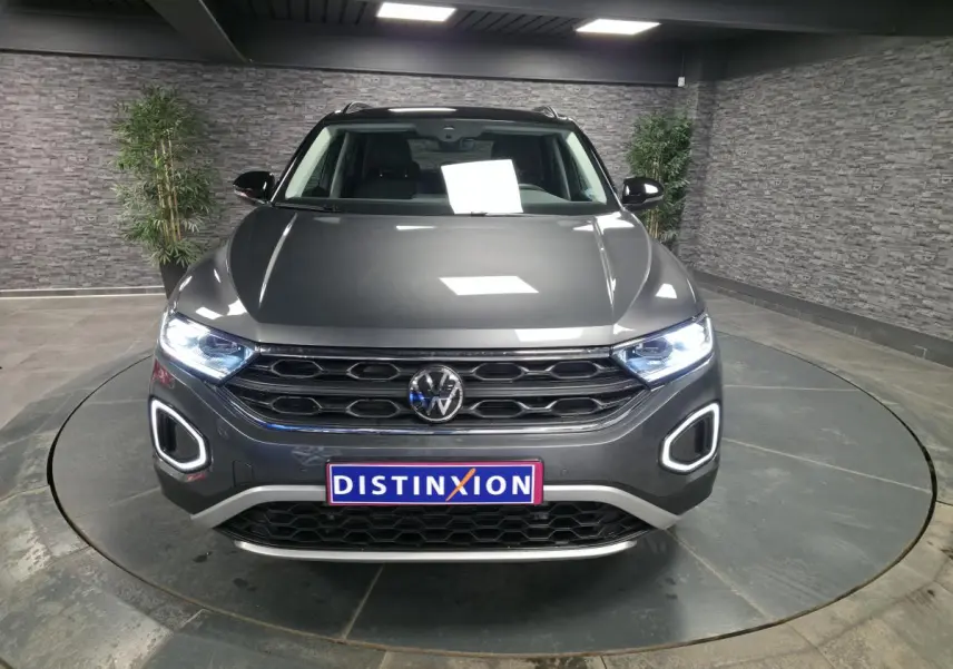 Vue de face d'un Volkswagen T-Roc gris métallisé avec feux LED allumés et calandre noire en showroom.