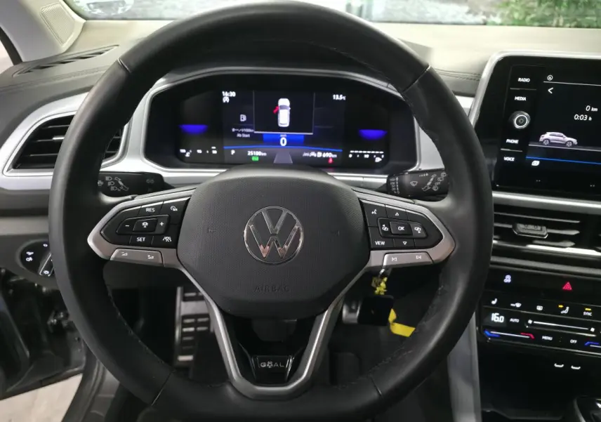 Vue intérieure centrée sur le volant noir du Volkswagen T-Roc gris avec tableau de bord digital et écran tactile.
