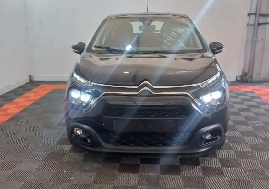 Vue frontale d'une Citroën C3 noire 2024 avec phares LED allumés dans un garage au sol damier.