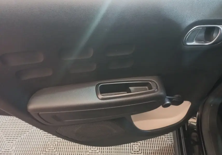 Vue rapprochée de la porte intérieure côté droit noire de la Citroën C3 2024 avec poignée et manivelle de vitre.