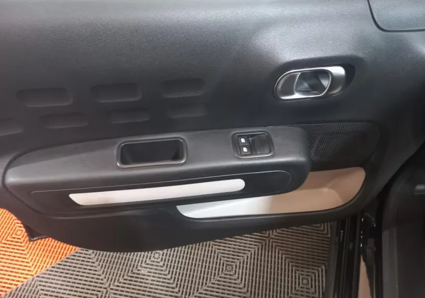 Vue intérieure de la porte côté conducteur de la Citroën C3 noire, avec commandes de vitres et poignée argentée.