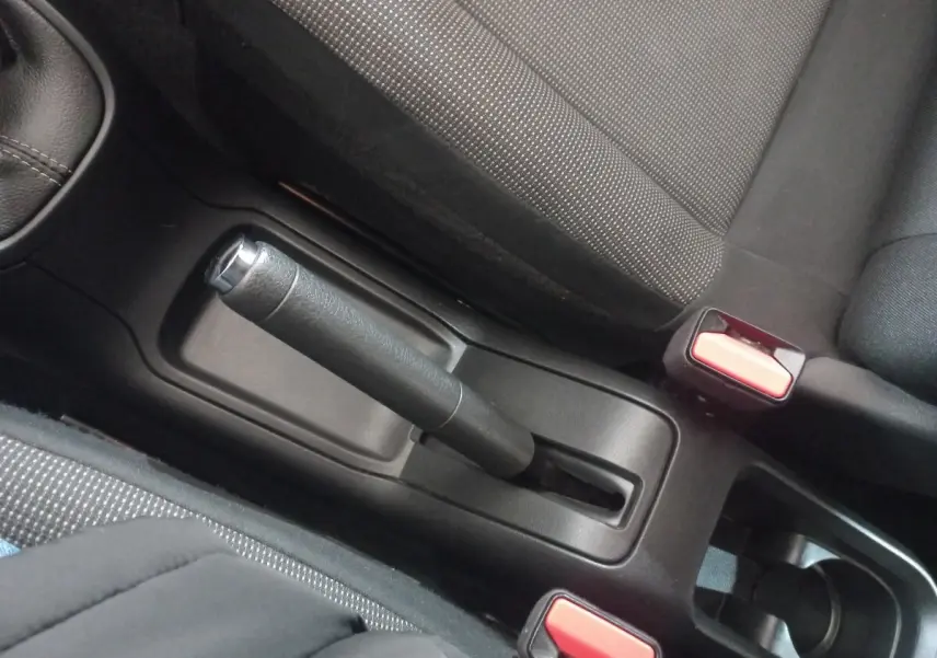 Vue rapprochée de la console centrale noire de la Citroën C3 2024, avec frein à main manuel et ceintures rouges.