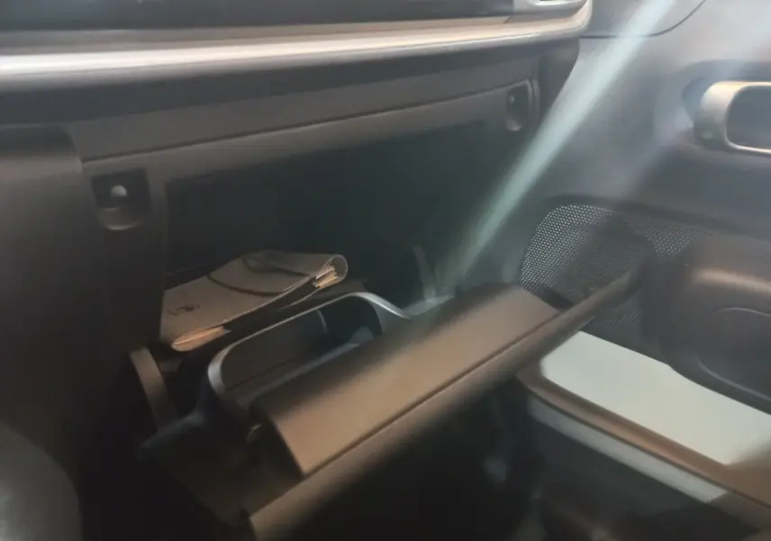 Intérieur de la Citroën C3 2024 noir, vue sur la boîte à gants ouverte côté passager avec rangement et document visible.