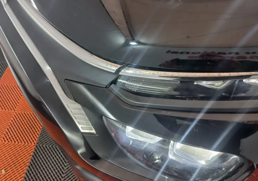 Gros plan sur le phare avant gauche noir brillant d'une Citroën C3 2024 avec détails chromés et éclairage LED.