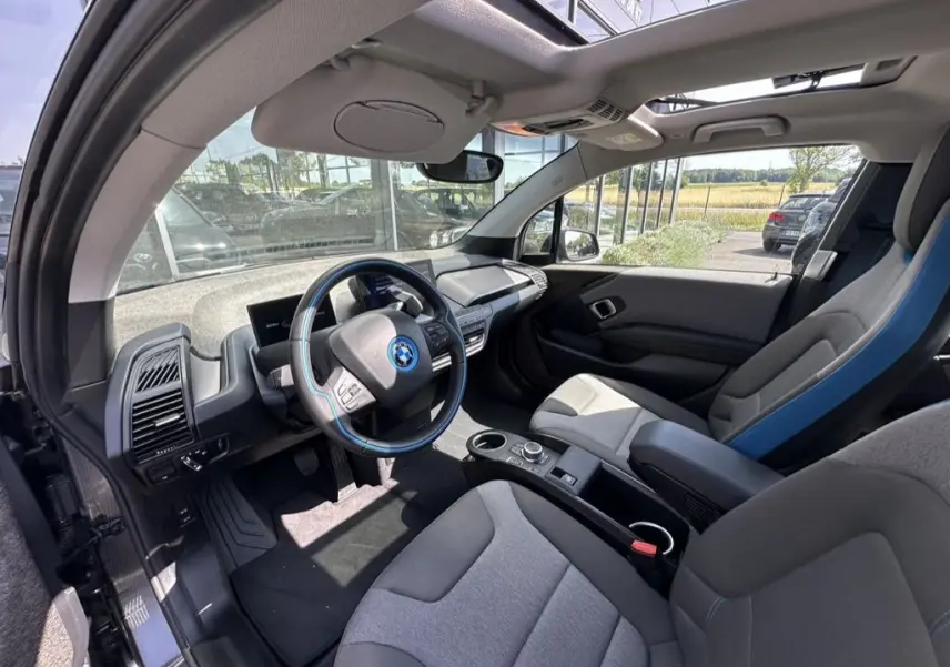 Intérieur de la BMW i3 2022 vu côté conducteur, avec volant bleu et sièges gris clair en tissu.