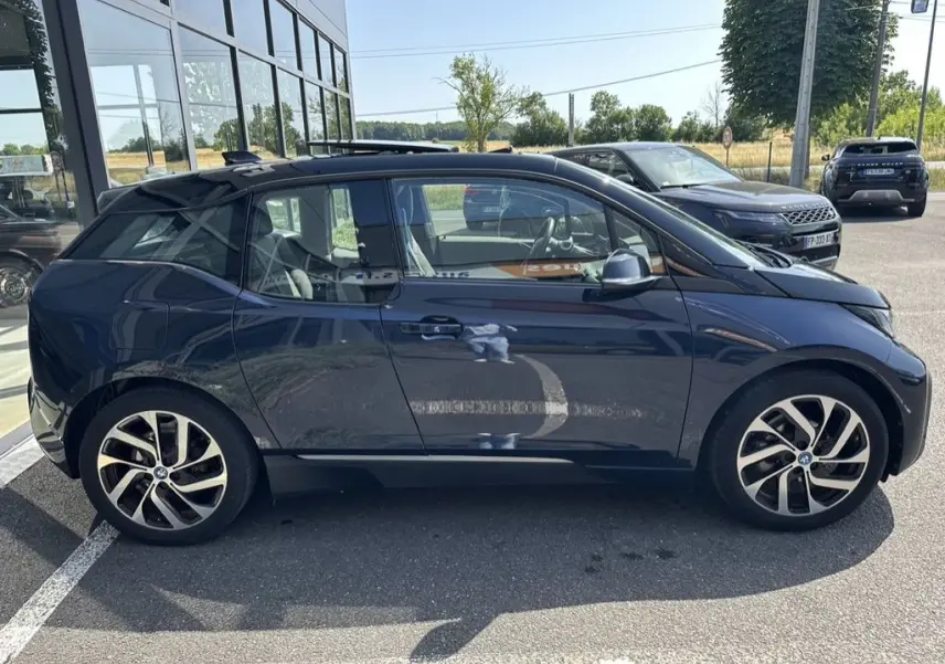 Profil côté gauche d'une BMW i3 électrique bleue 2022, avec ses jantes distinctives en alliage et toit noir.