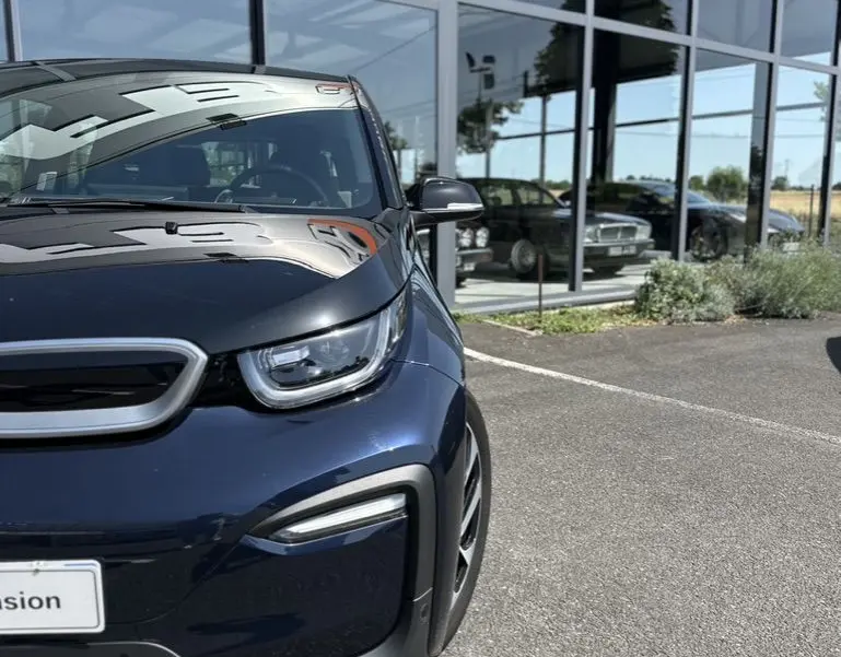 Vue 3/4 avant gauche d'une BMW i3 électrique bleue 2022 stationnée devant une vitrine de concession.