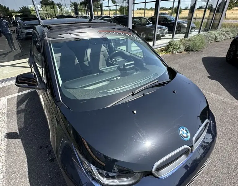 BMW i3 électrique bleue vue en 3/4 avant avec toit noir brillant et logo BMW visible sur le capot.