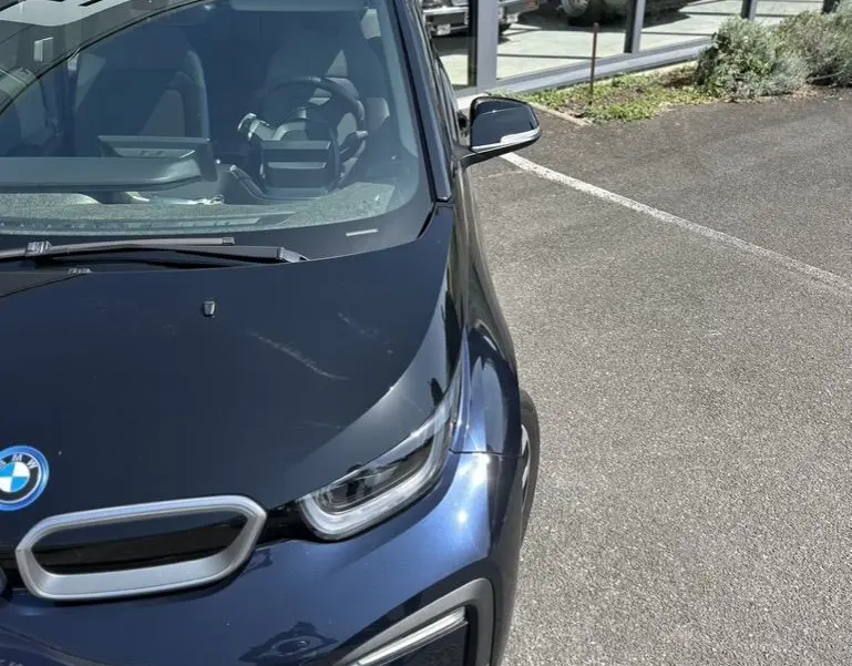 Vue 3/4 avant droite d'une BMW i3 bleue électrique 2022, avec ses phares LED et calandre caractéristique visibles.
