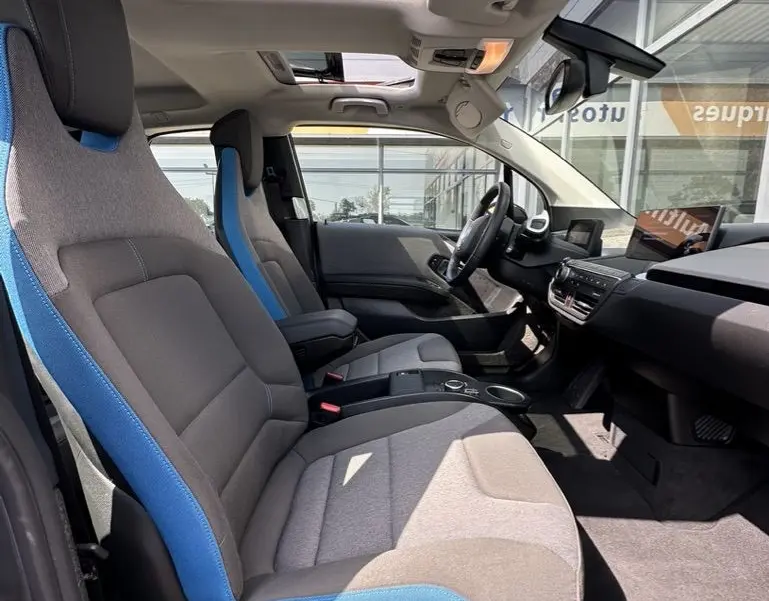 Intérieur de la BMW i3 2022 vue côté droit, sièges gris avec surpiqûres bleues et toit ouvrant panoramique.