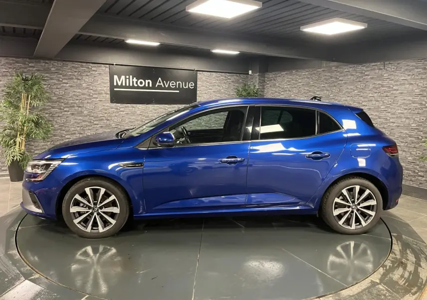Profil côté gauche de la Renault Mégane hybride rechargeable bleu Iron avec jantes alliage 17 pouces en intérieur showroom.