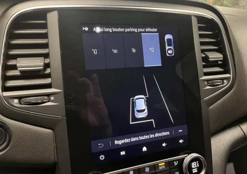 Écran tactile central de la Renault Mégane hybride bleue affichant l'assistance au stationnement en vue intérieure.
