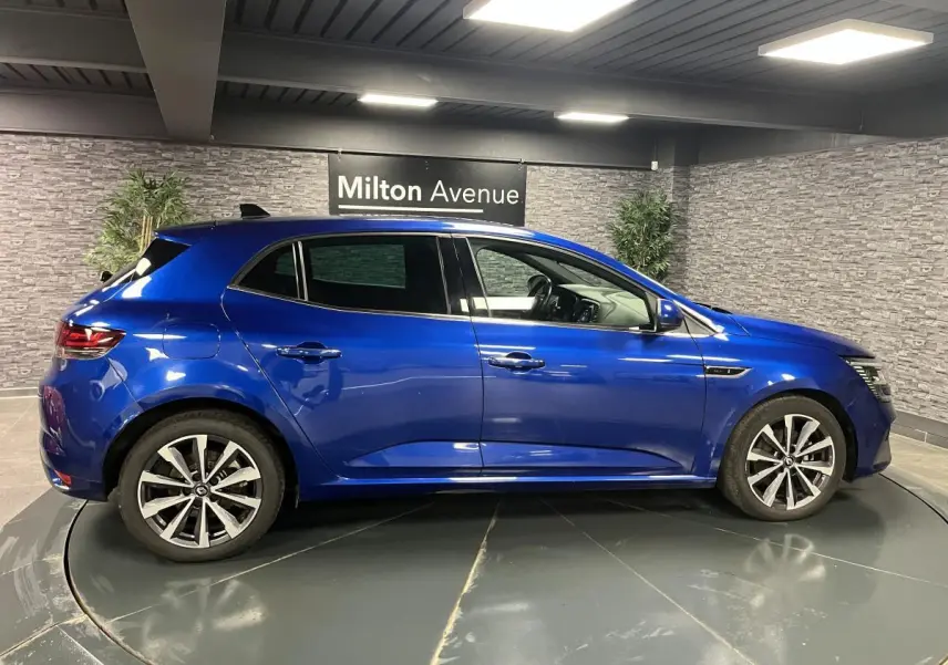 Profil côté gauche de la Renault Mégane hybride rechargeable bleu Iron avec jantes alliage 17 pouces en intérieur showroom.